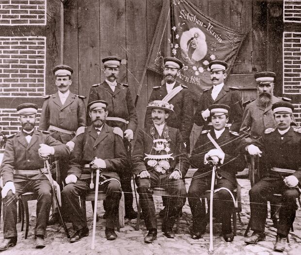Das älteste erhaltene Foto der Schützenbruderschaft St. Johannes Wimbern zeigt Vorstand und König im Jahre 1903/04. Der Schützenkönig regierte damals noch ohne eineKönigin. Die Aufnahme entstand auf dem Hof Goeke und zeigt vor der Deelentür die Fahne von 1893 sowie folgende Personen: Hintere Reihe, von links: Wilhelm Sturzenhecker (Oesbern), Heinrich Schulte (Werringsen), Fritz Knieper (Wimbern), Josef Schüpstuhl (Wimbern) und Franz Brune (Brockhausen). Vordere Reihe, von links: Josef Coerdt gen. Nadermann (Wimbern), Oberst und Gemeindevorsteher Anton Goeke (Wimbern) sowie König Heinrich Beringhoff, Josef Goeke (Wimbern) und Max Stratmann (Bellingsen).  FOTO: BILDARCHIV VEREIN DORF WIMBERN