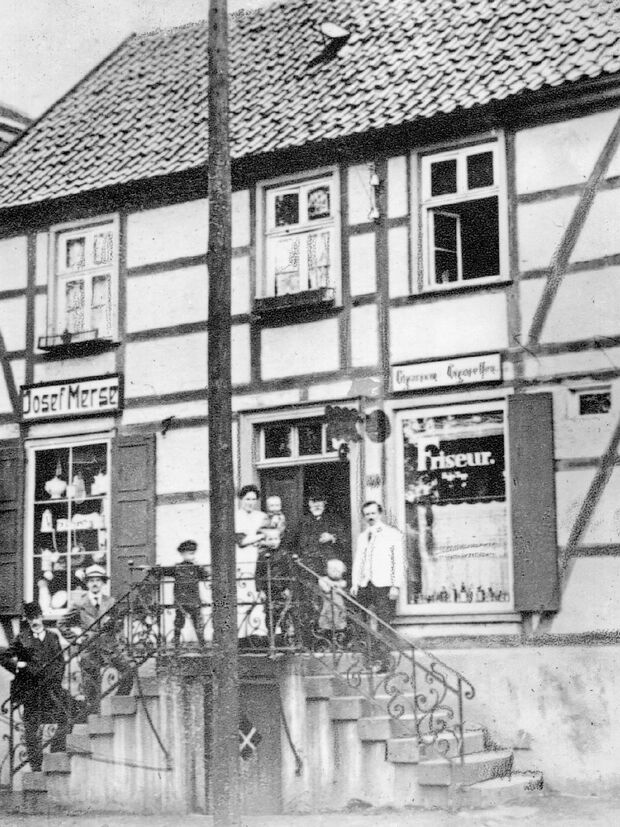 Das alte Fachwerkhaus Merse an der Hauptstraße in einer historischen Ansicht: Neben dem Geschäft von Josef Merse (links) ist auf der anderen Seite des Hauses ein „Friseur“ mit seinem Salon zu erkennen. Das Gebäude hatte damals noch einen zweiflügeligen Treppenaufgang und eine Fachwerkfassade, die heute hinter einer Verkleidung aus Putz und anderen Materialien verschwunden ist. FOTOGRAF: UNBEKANNT / REPRODUKTION: ANDREAS DUNKER